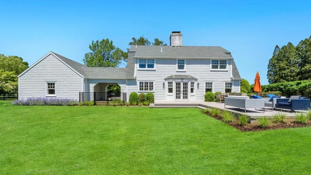 A large house stands behind a broad green lawn, with a patio beside it.