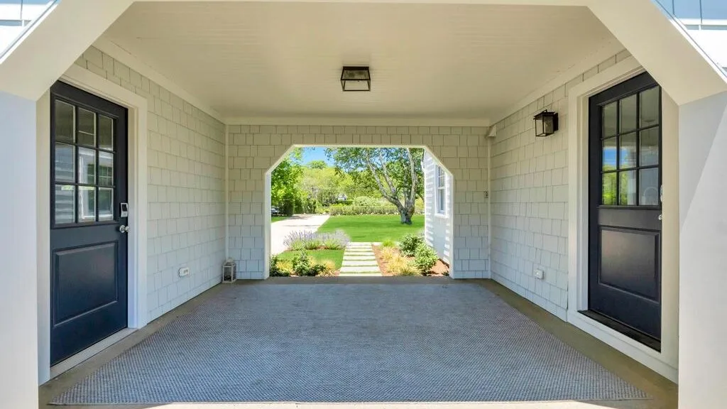 A covered porch with two dark doors and a garden visible beyond.
