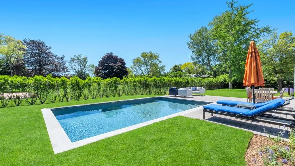 An outdoor swimming pool beside a lawn and a raised deck with lounge seating.