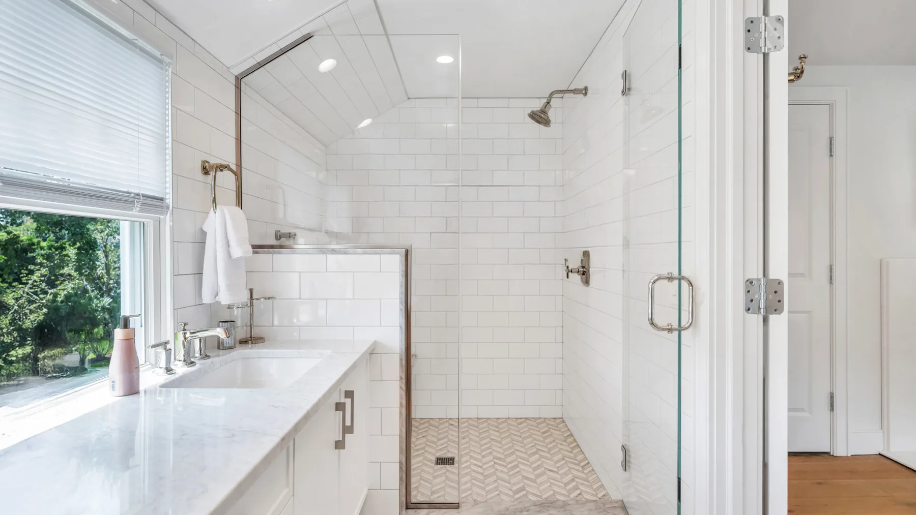 A bright bathroom with a tiled shower and a long vanity beside a window.