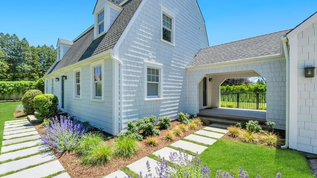A white house with a covered passage opening onto a garden and lawn.