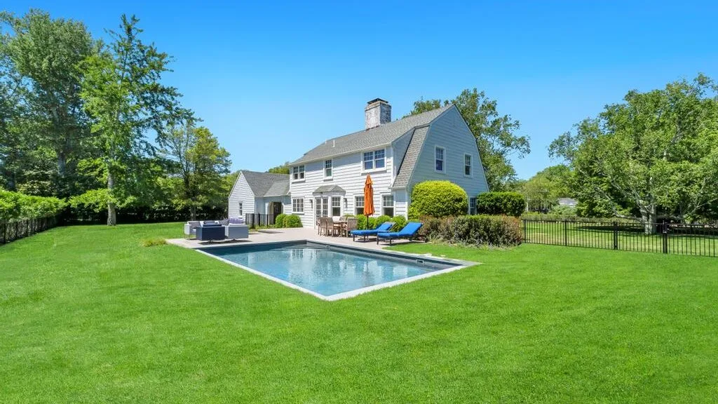 A house stands beside a swimming pool in a broad green lawn.