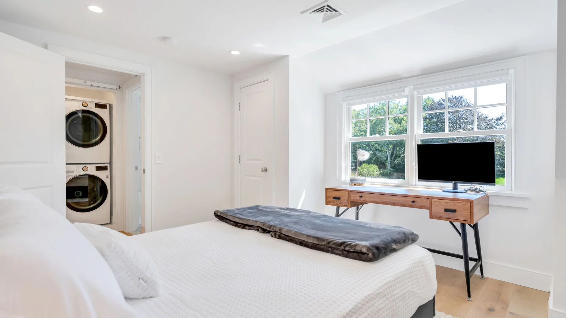 A bright bedroom with a bed, a desk, and a large window.
