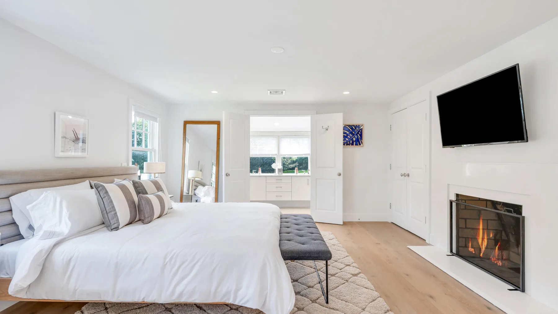 A bright bedroom with a neatly made bed, a television, and a fireplace.