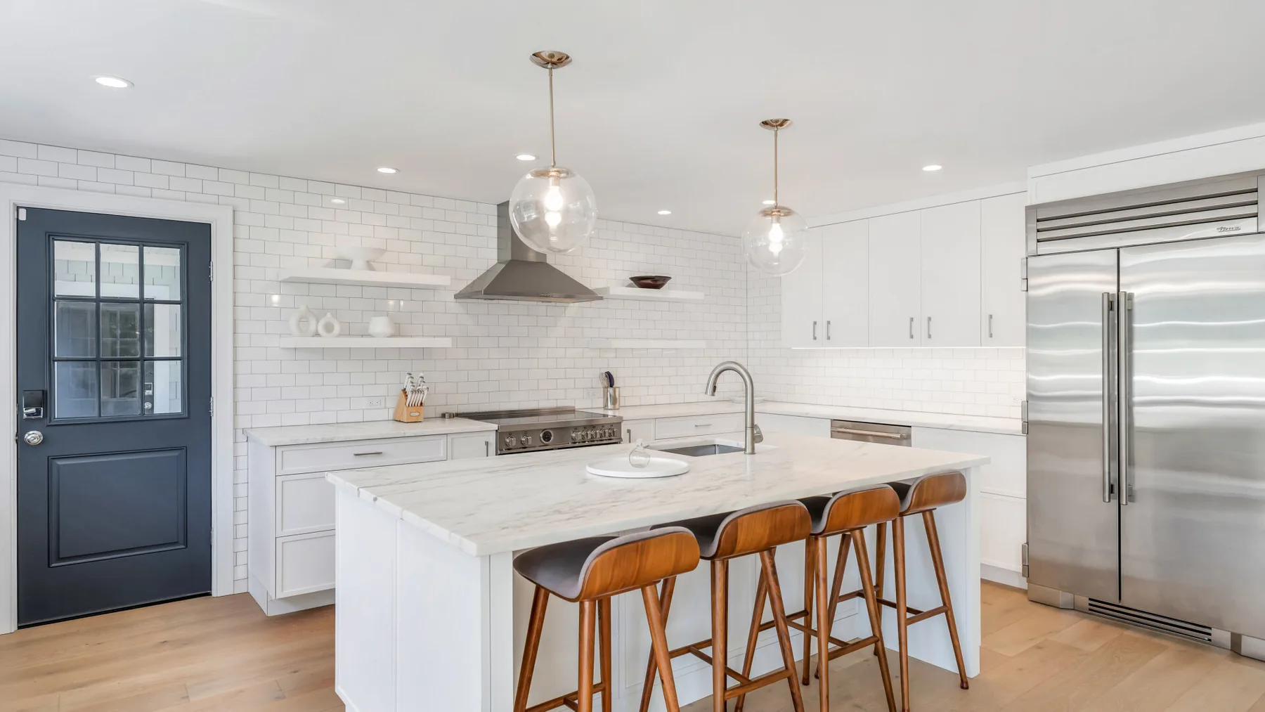 A bright kitchen with a white island, wooden seating, and stainless steel appliances.