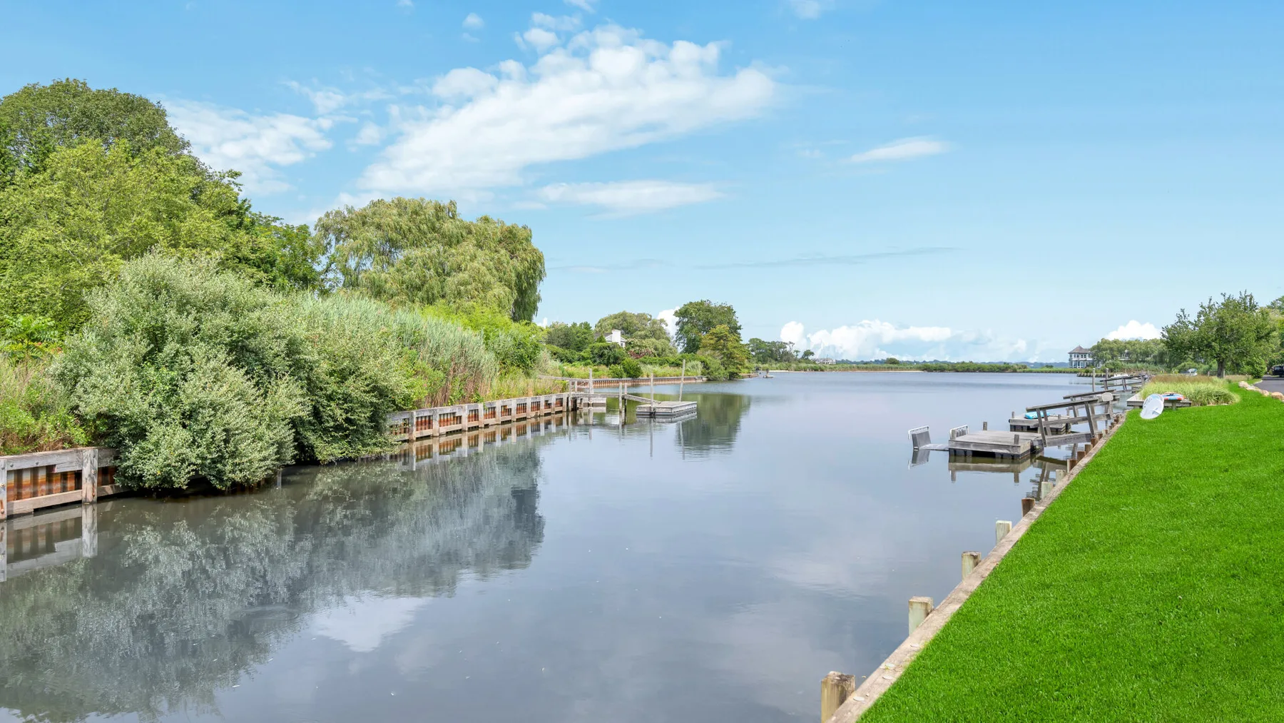 A calm waterfront scene with a grassy bank, trees, and small docks.