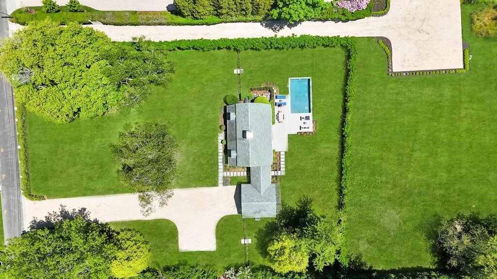 An aerial view shows a landscaped lawn, a small building, and a rectangular pool.