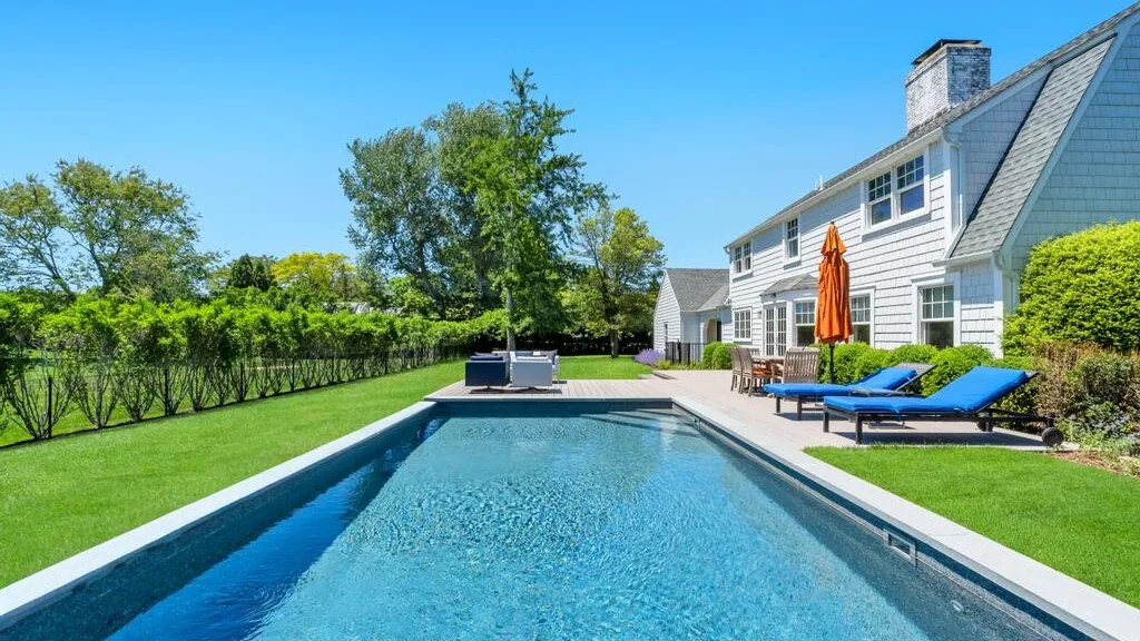 Outdoor swimming pool beside a house, with lounge seating on the patio.