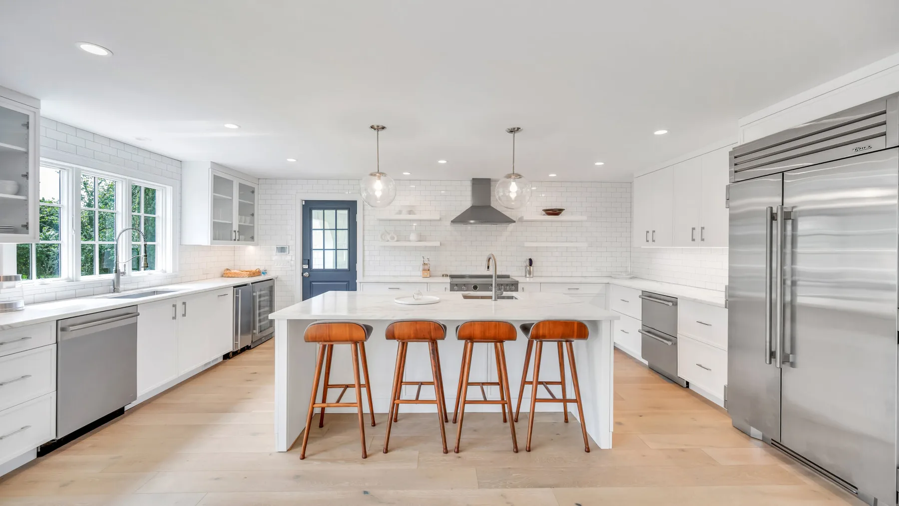 A bright kitchen with a central island and wooden stools.