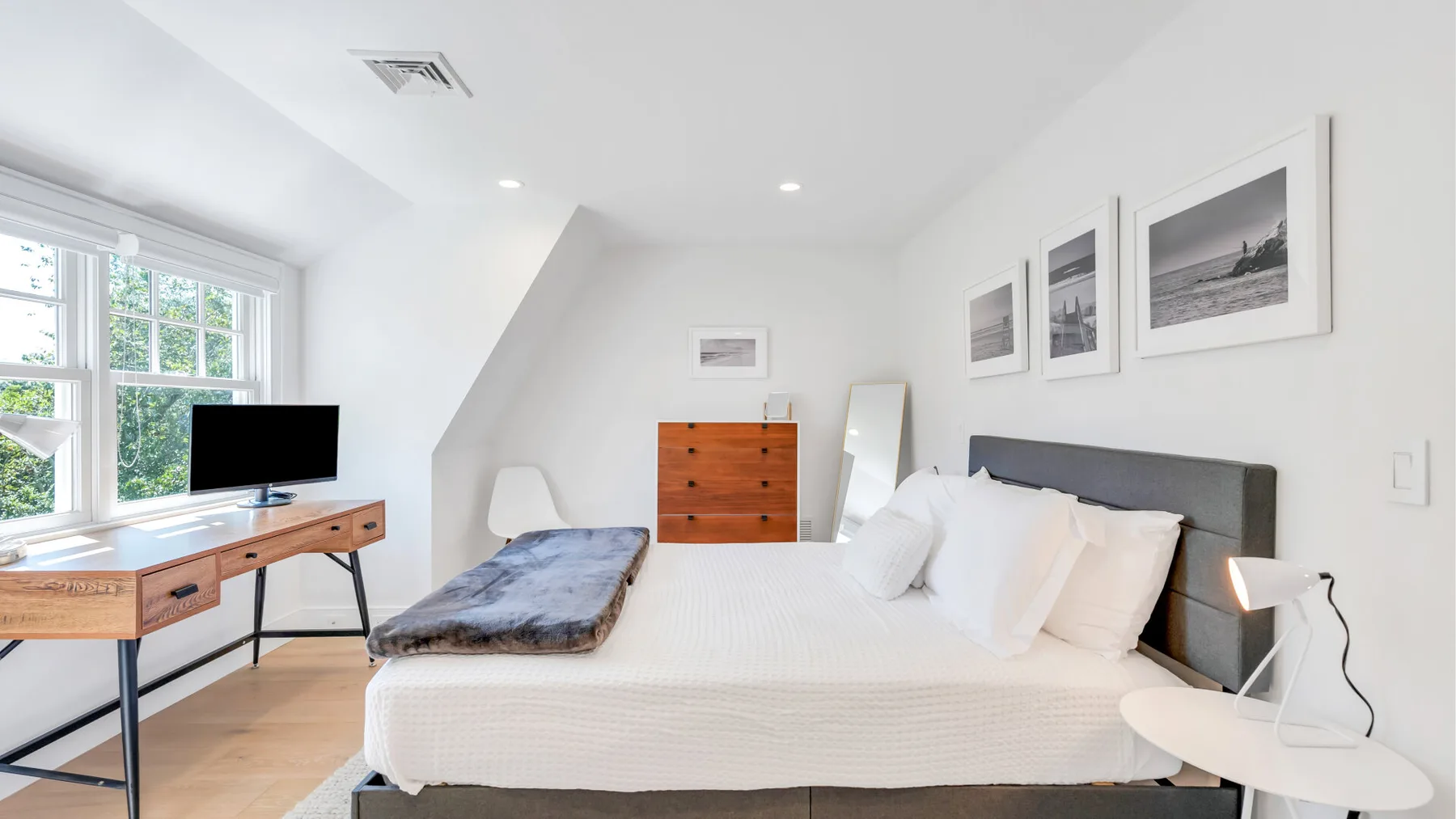 A bright bedroom with a large bed, a desk, and framed pictures on the wall.