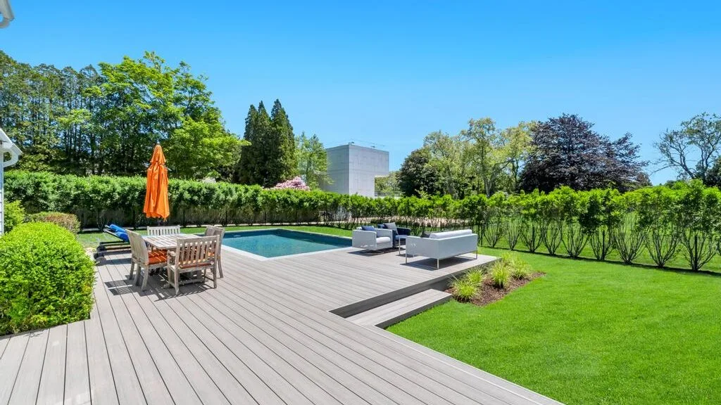 An outdoor pool area with a wooden deck, seating, and green lawn.