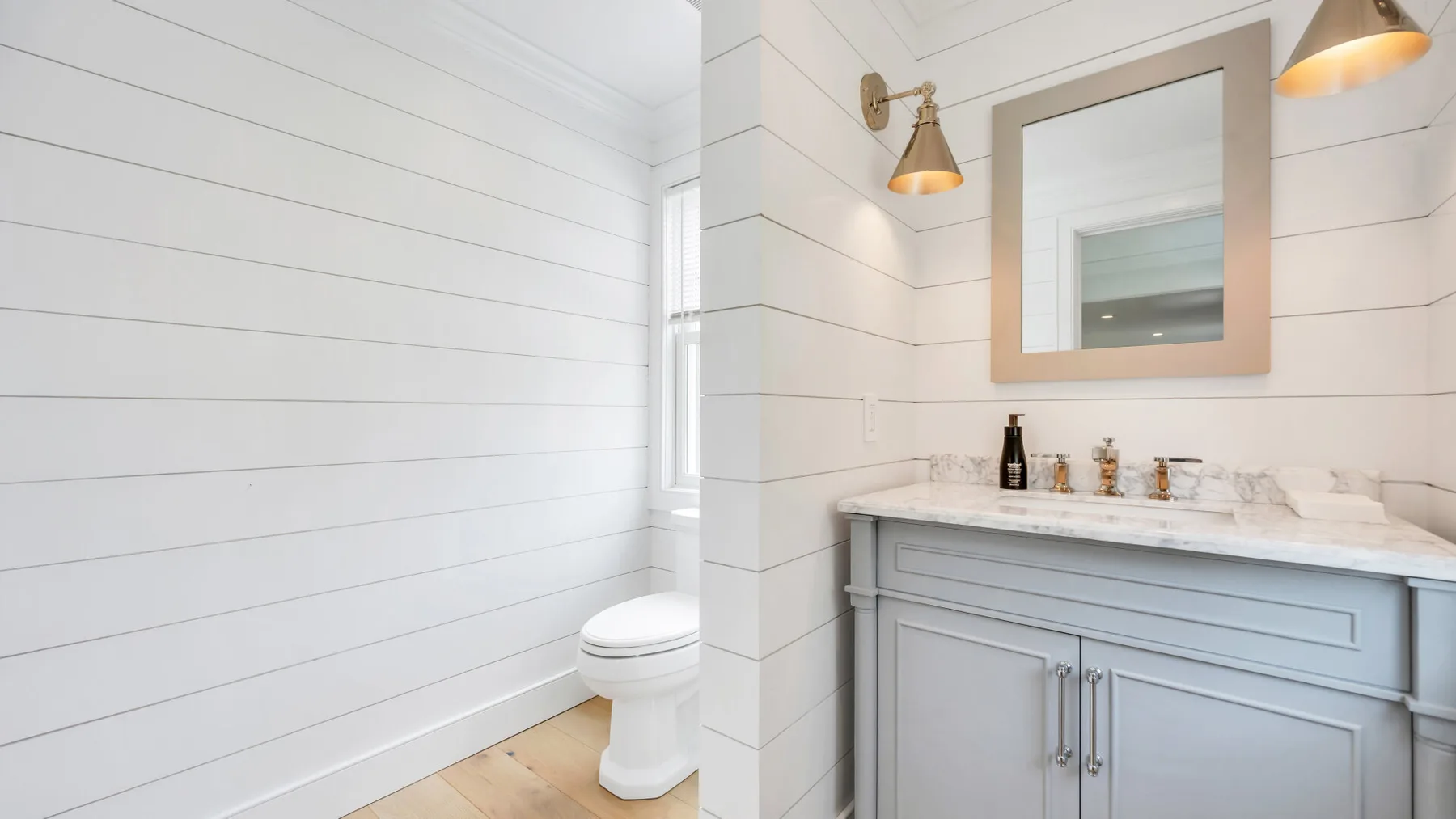 A bright bathroom with a toilet, vanity, and wall mirror.