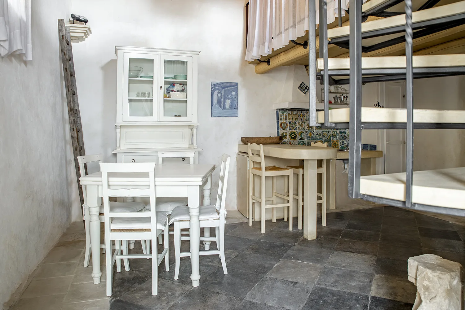 A dining area with a white table and chairs beneath a raised bed.