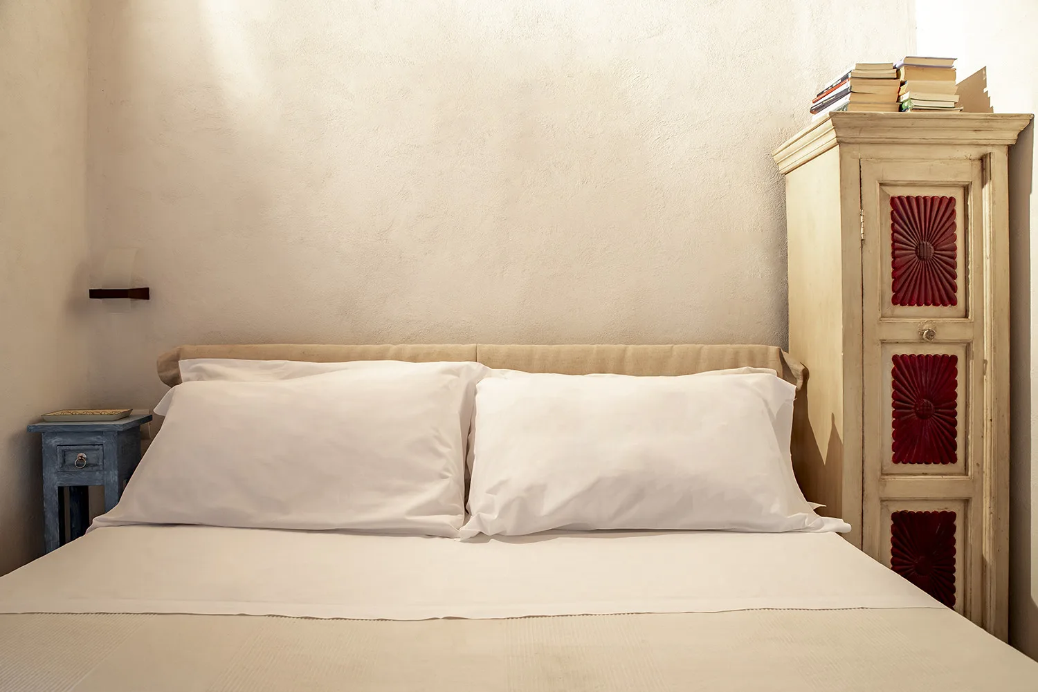 A bedroom with a neatly made bed and a tall wooden cabinet.