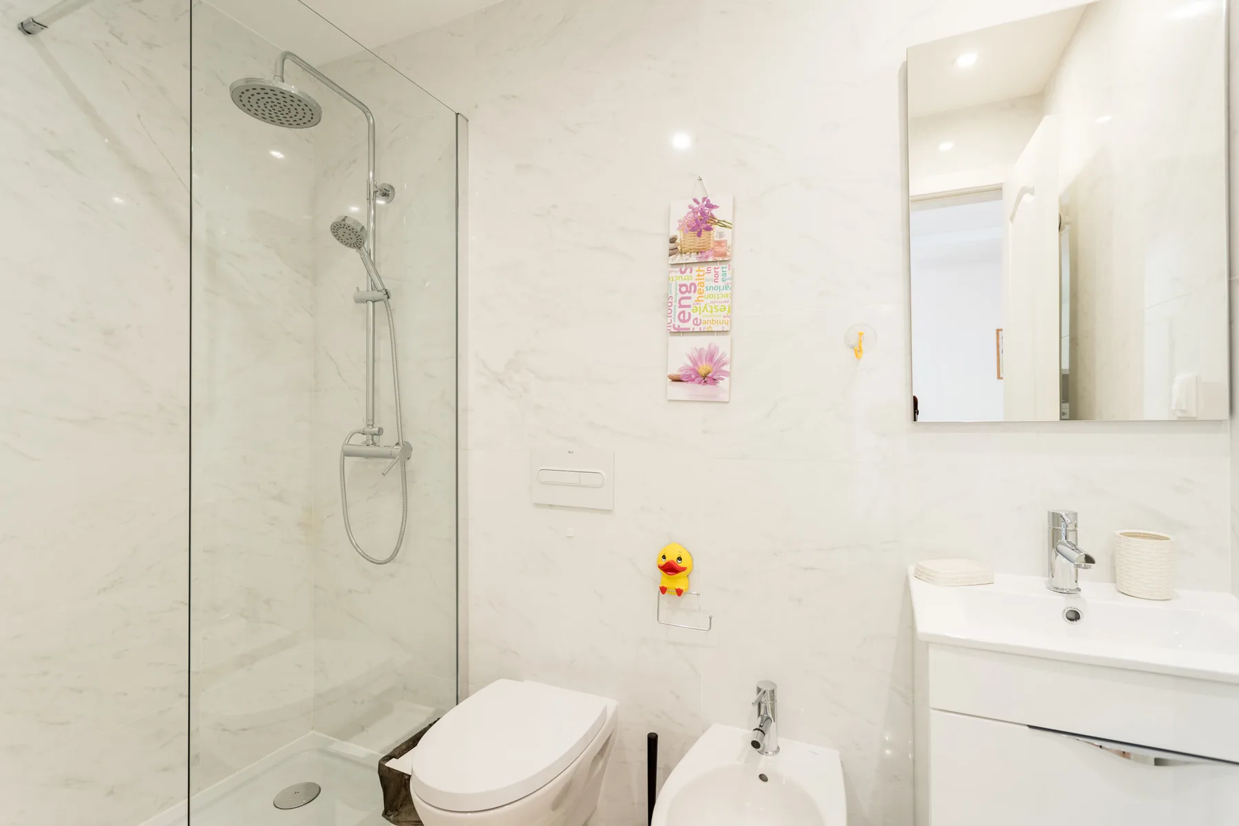 Un baño luminoso con ducha de vidrio, inodoro y lavabo.