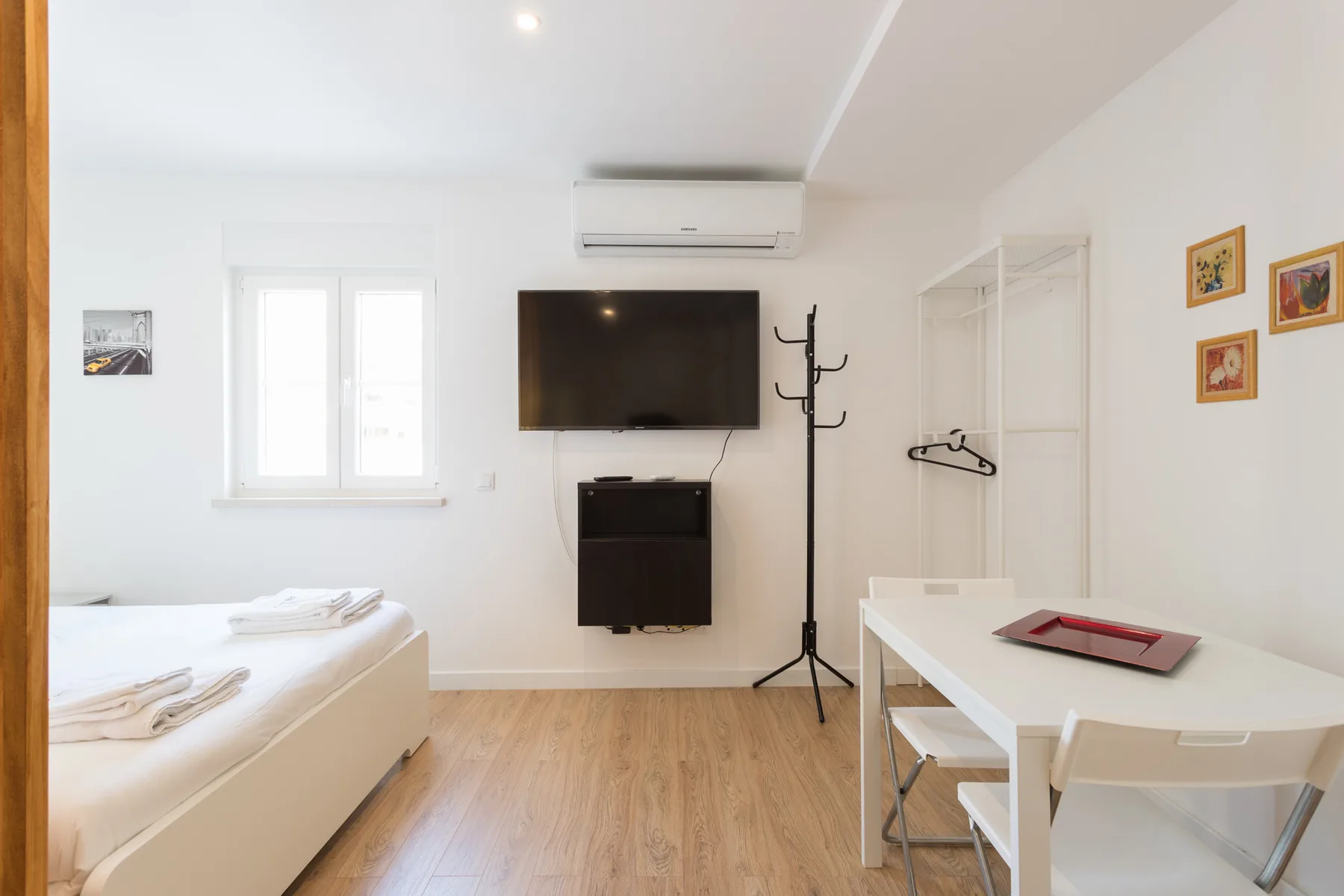 Un dormitorio luminoso con camas, un televisor y una mesa de comedor.