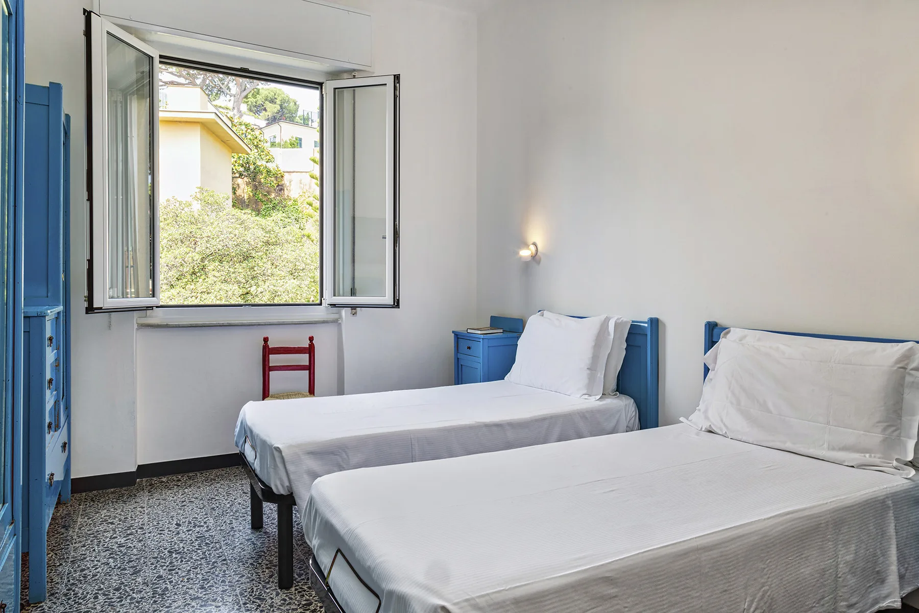 Un dormitorio con dos camas y una ventana abierta con vistas a la vegetación.