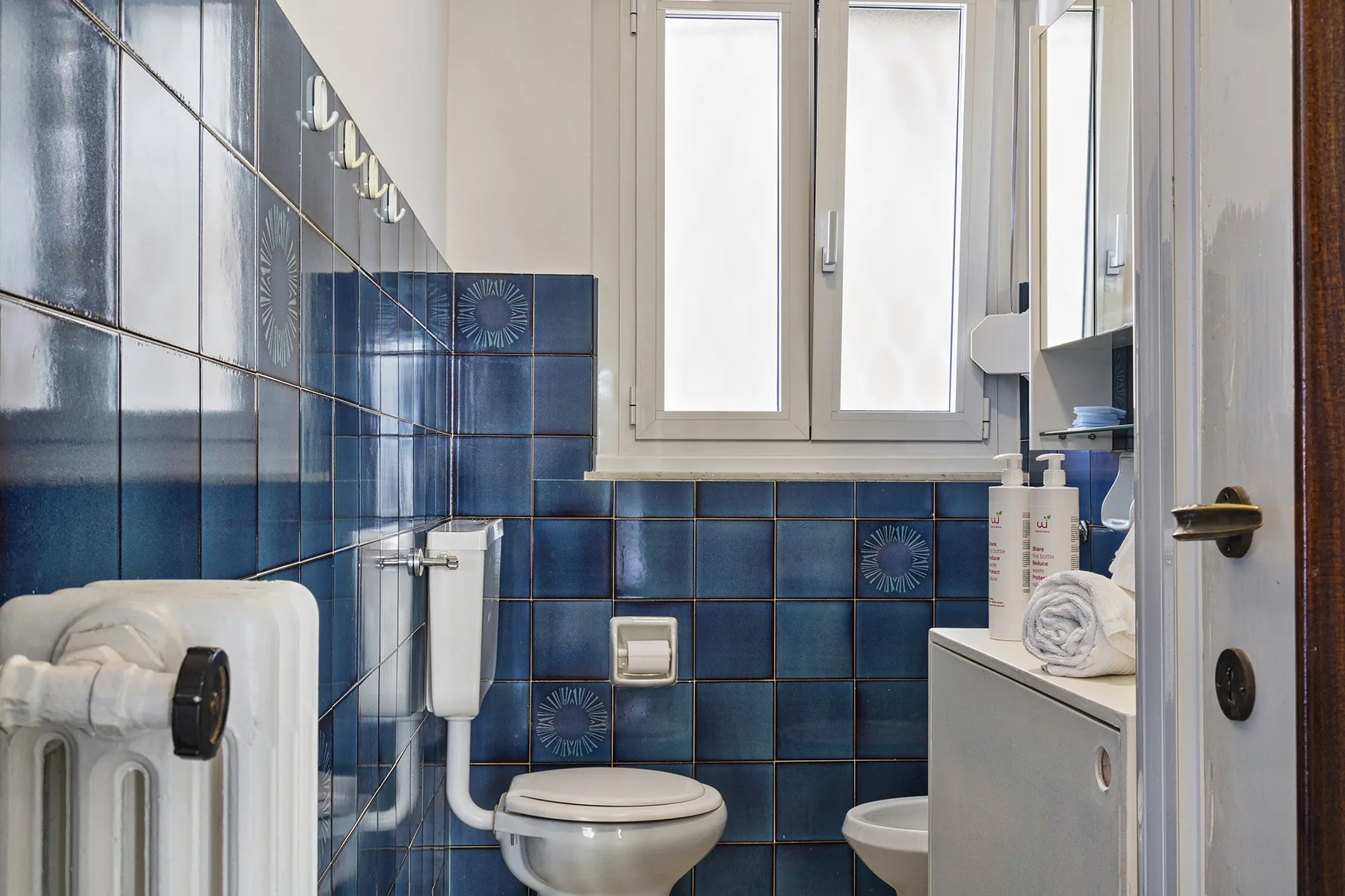 Un baño alicatado con inodoro, lavabo y ventana.