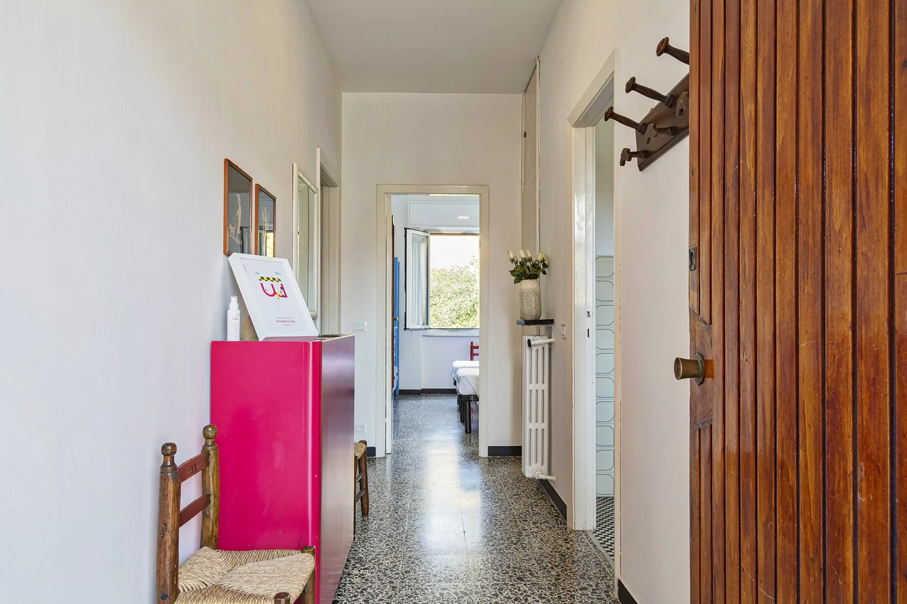 Un pasillo estrecho con un mueble rosa intenso y una puerta al fondo.
