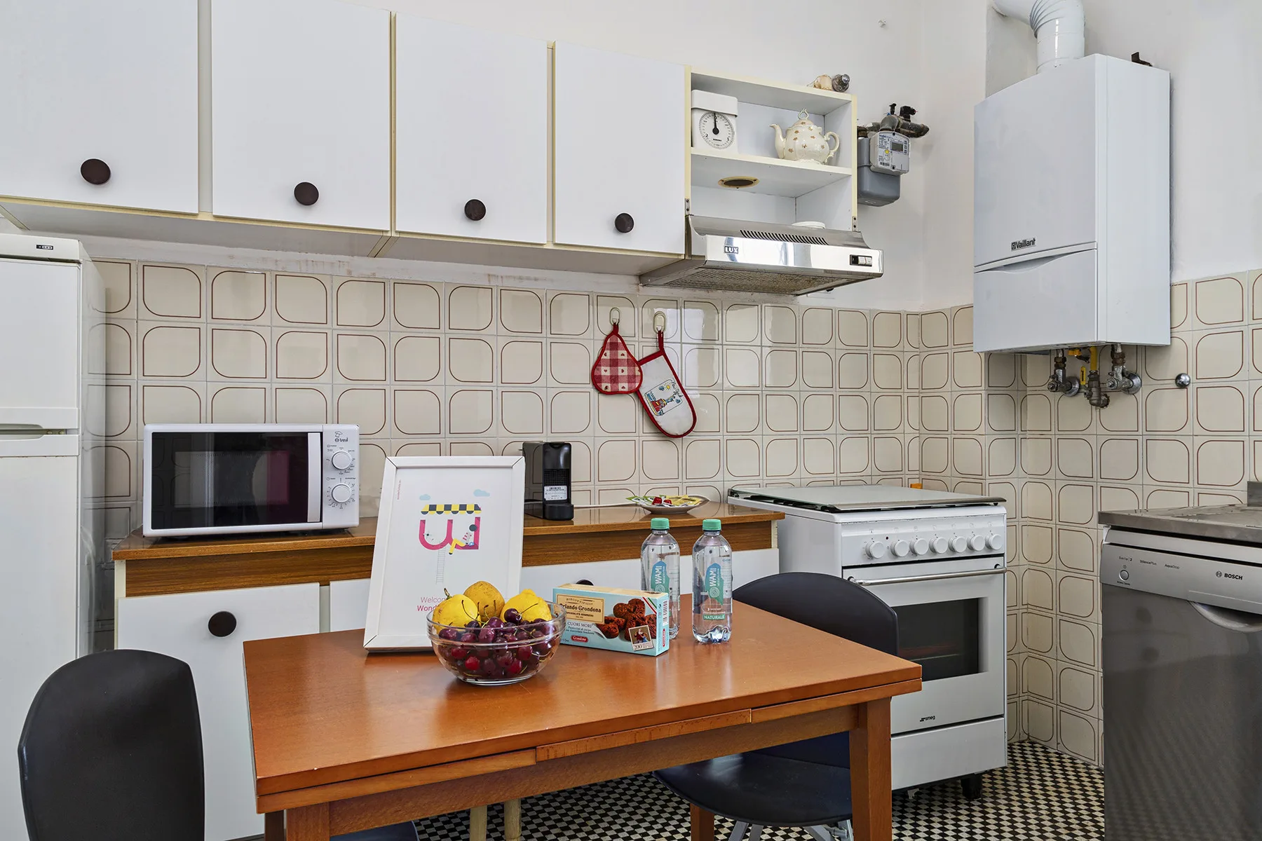 Una cocina con una mesa de madera, microondas, estufa y salpicadero de azulejos.