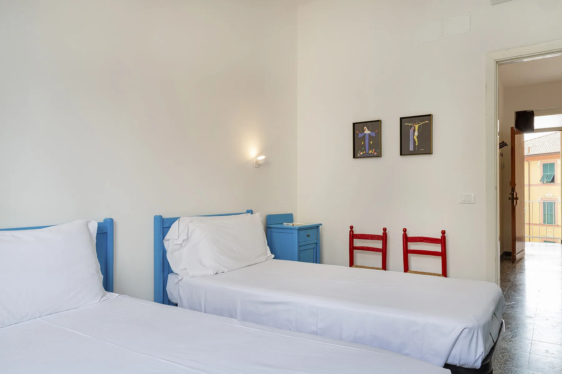 Un dormitorio luminoso con camas, sillas rojas y cuadros en la pared.
