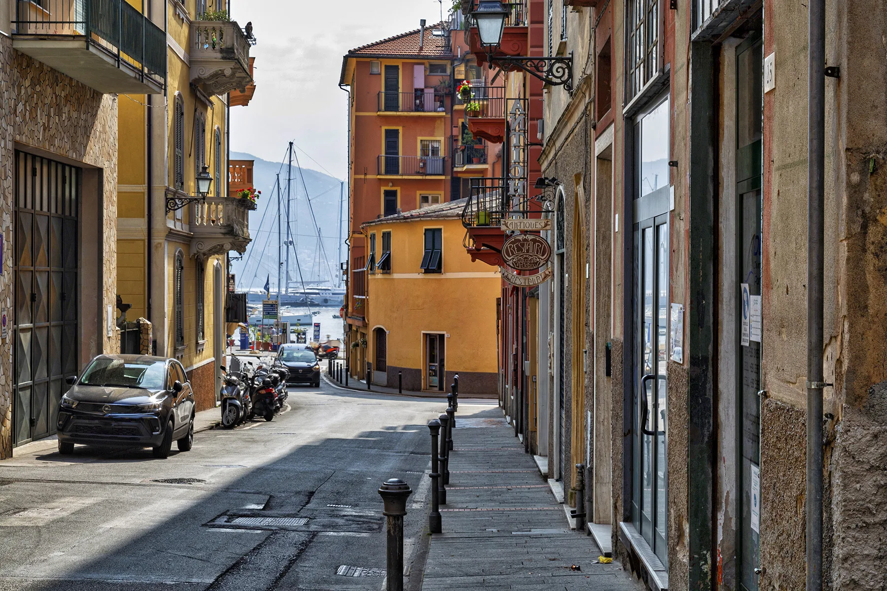 Una calle estrecha bordeada de edificios coloridos conduce a un puerto con veleros.