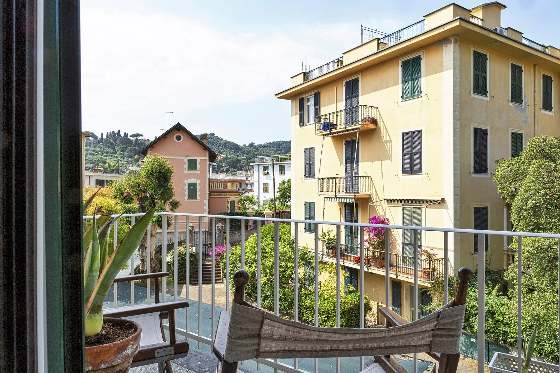 Un balcón da a edificios de apartamentos cercanos y colinas verdes.