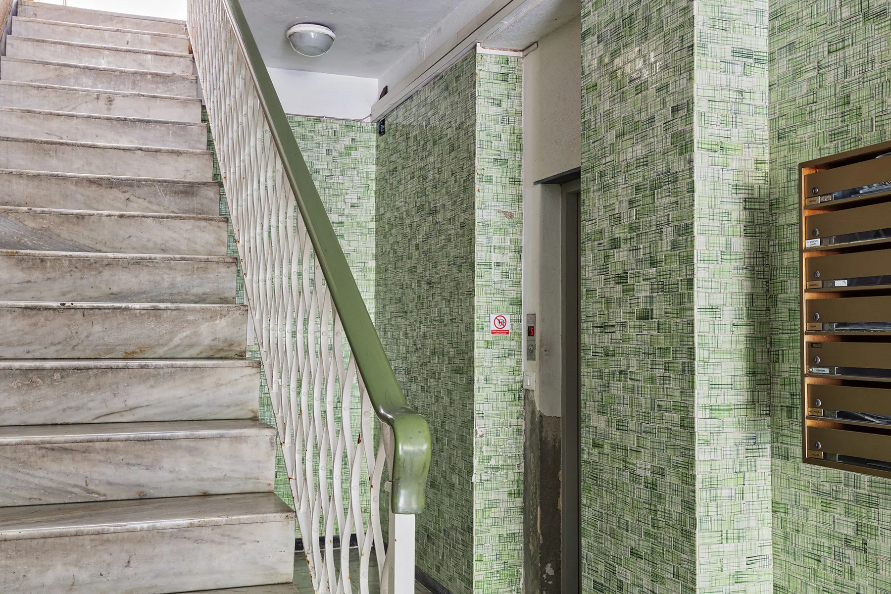 Una escalera con paredes revestidas de azulejos y un conjunto de buzones.