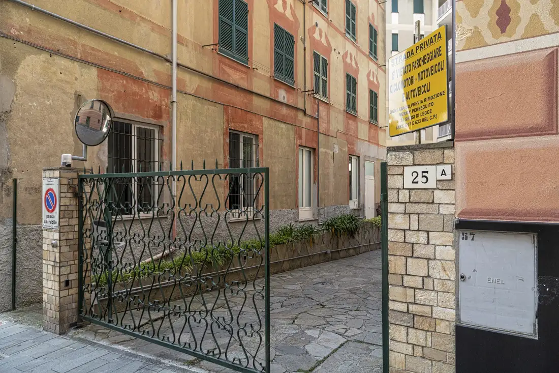 Un pasaje exterior pavimentado de piedra discurre entre edificios envejecidos y una verja metálica.
