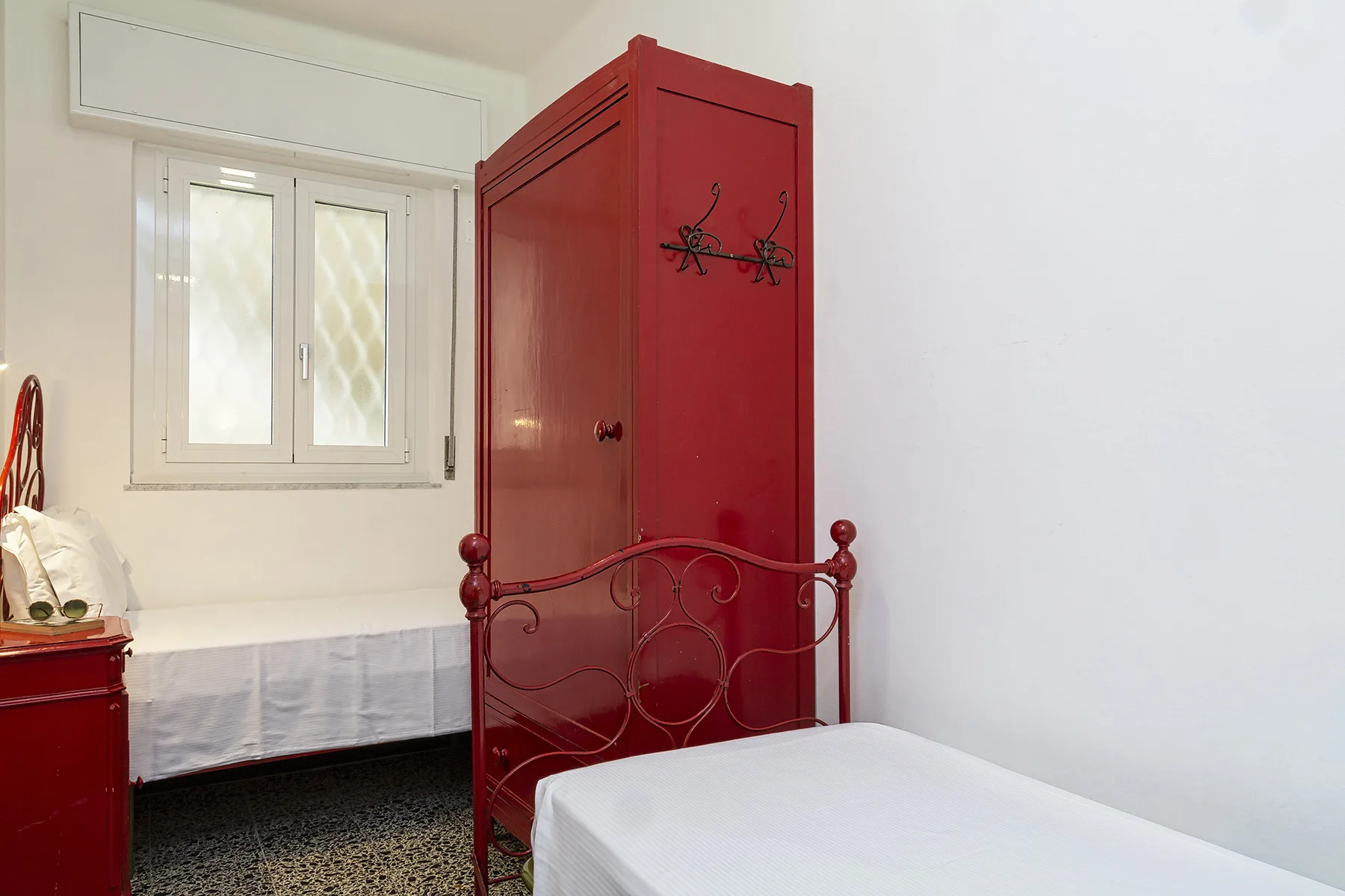 Un dormitorio con un armario rojo junto a una cama y una ventana.