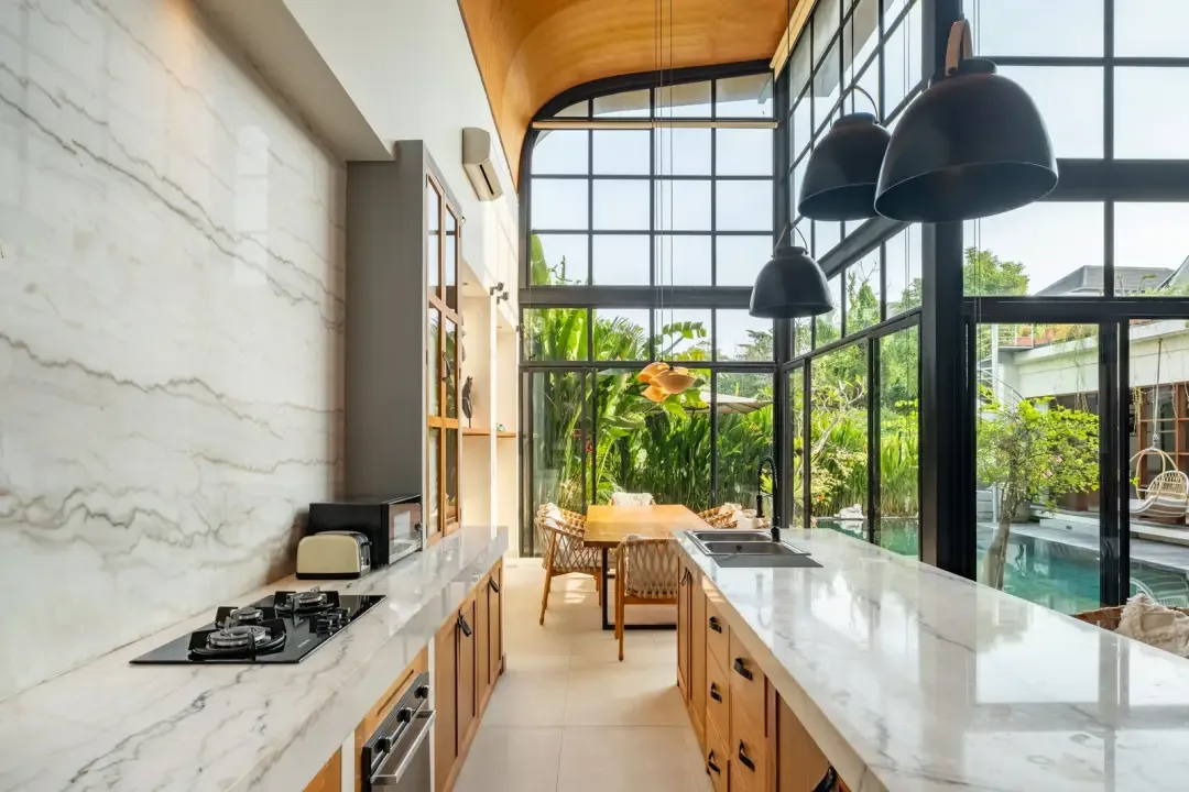 A bright kitchen with marble counters and large windows overlooking greenery.