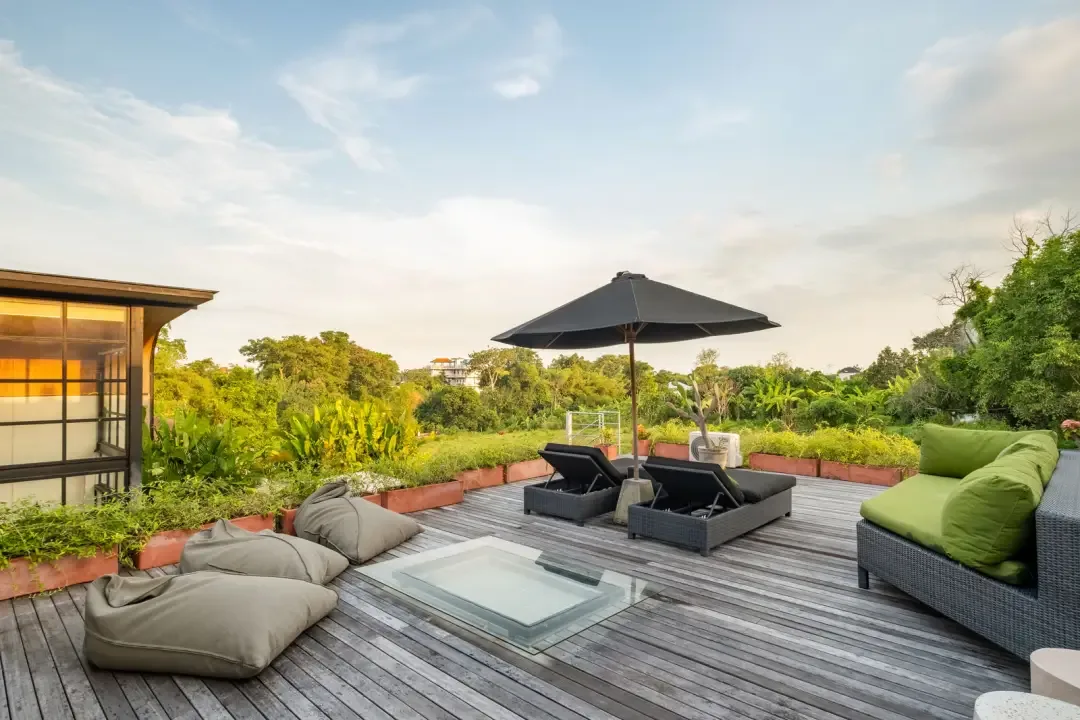 An outdoor deck seating area surrounds a glass-covered feature beneath a sun umbrella.