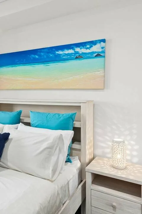 Un dormitorio con una cama blanca, almohadas turquesas y una imagen de playa sobre el cabecero.