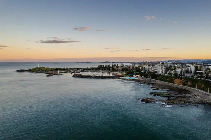 La costa se curva junto a edificios y aguas tranquilas al atardecer.