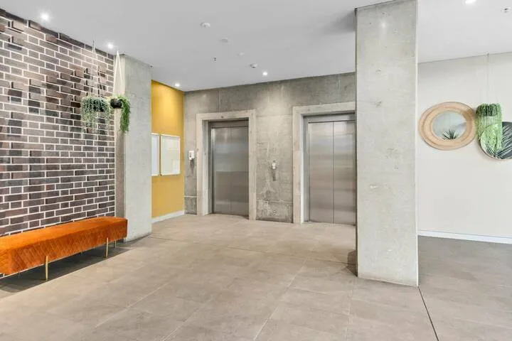 Un vestíbulo interior con dos puertas de ascensor y un banco junto a la pared de ladrillo.