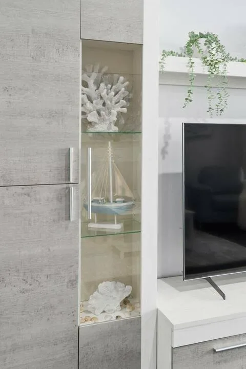 Un mueble moderno de sala exhibe coral decorativo y un velero en miniatura junto a un televisor.