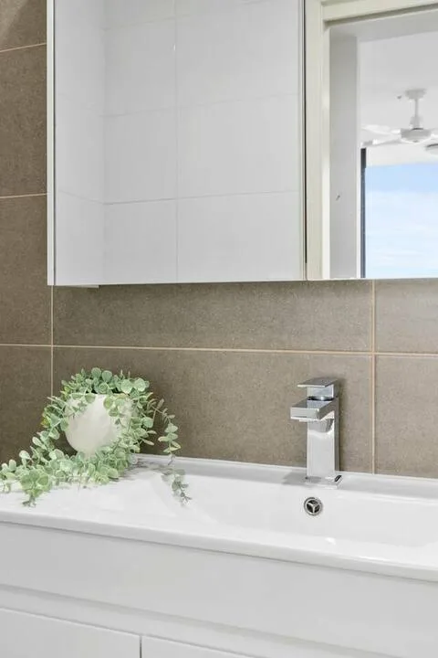 Un lavabo de baño con fregadero blanco, salpicadero de azulejos y armario con espejo.