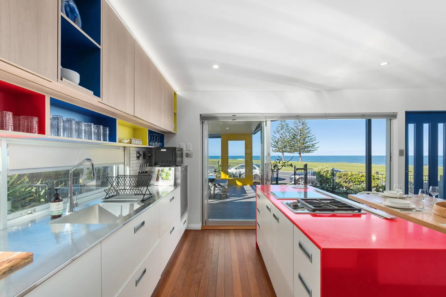 Una cocina luminosa con una isla roja y amplias puertas de vidrio que dan a un patio.