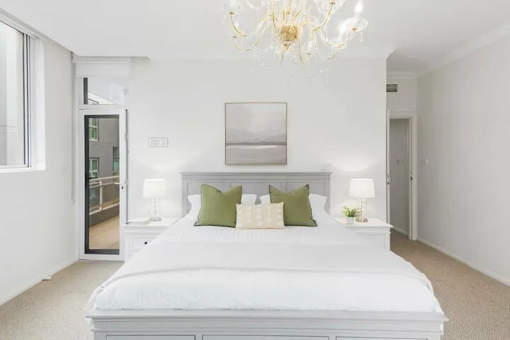 Un dormitorio luminoso con una cama blanca y cojines decorativos verdes.
