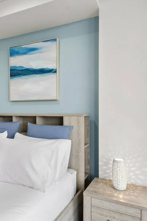 Un dormitorio con una cama, una pared azul y un cuadro de paisaje.