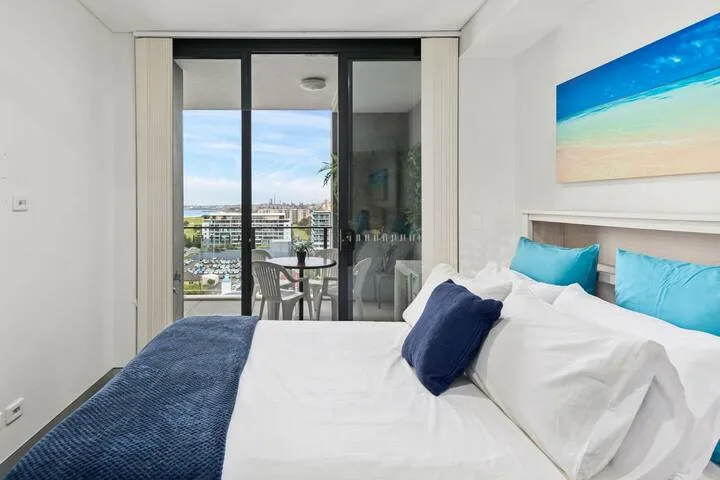 Un dormitorio con ropa de cama blanca y puertas corredizas de vidrio que dan a un balcón.
