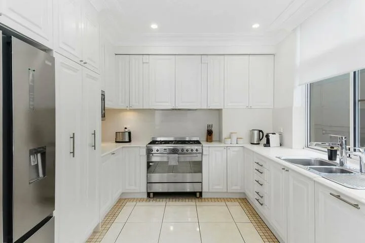 Una cocina blanca y luminosa con refrigerador y horno de acero inoxidable.