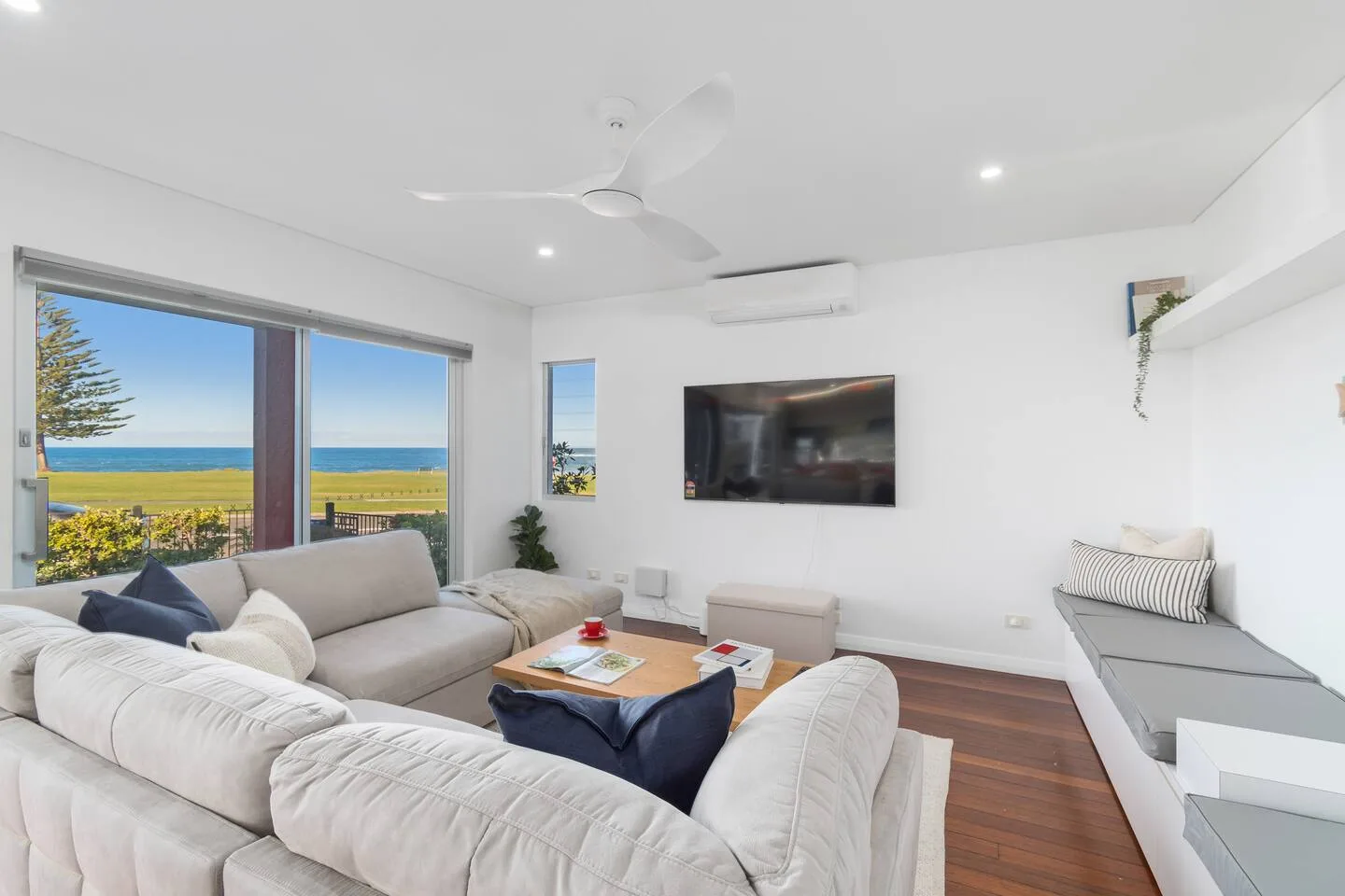 Una luminosa sala de estar con asientos frente a grandes ventanales con vistas al mar.