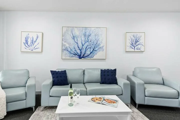 Una sala luminosa con asientos claros y arte botánico azul en la pared.