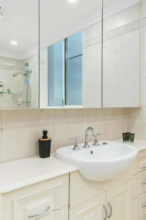 Un baño con azulejos, lavabo, armarios con espejo y ducha.