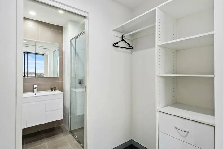 Un vestidor con estantes abiertos junto a un lavabo y una ducha.