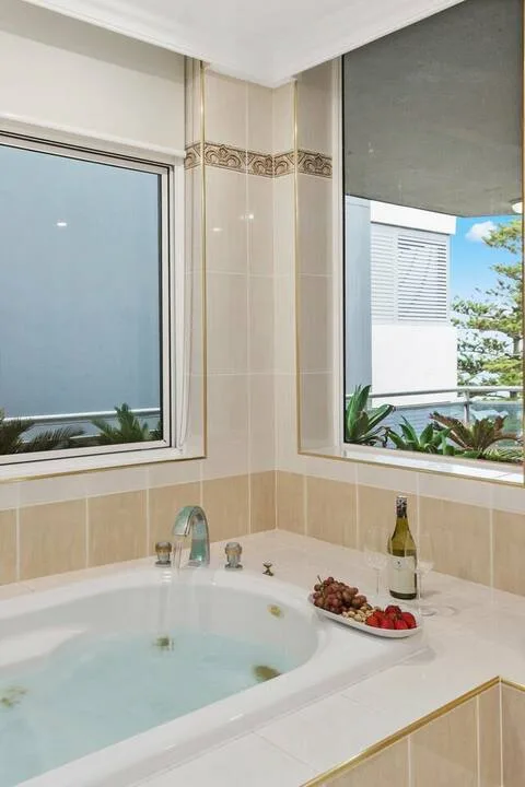 Una esquina de baño cuenta con una bañera empotrada bajo dos ventanas.