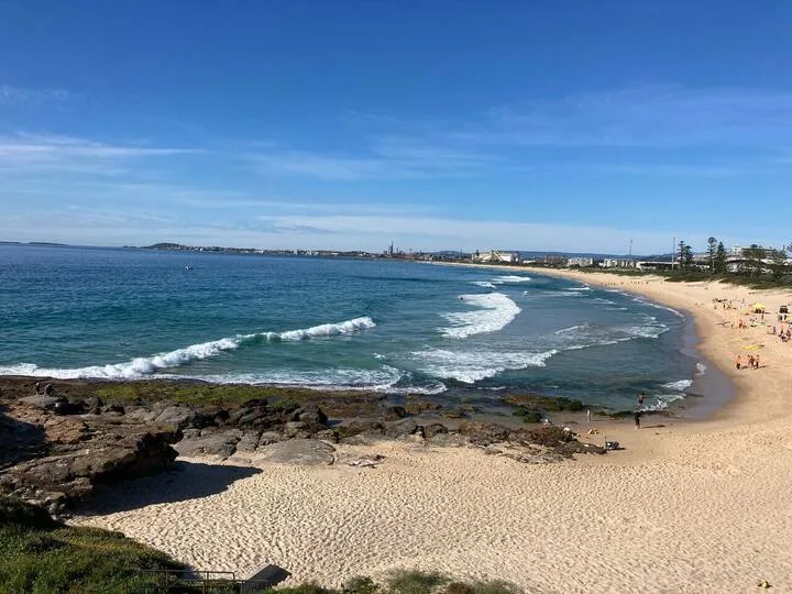 Una playa de arena bordea una bahía mientras pequeñas olas rompen en la orilla.