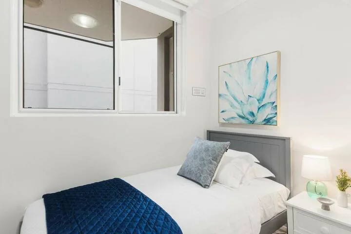 Un dormitorio luminoso con una cama tendida y ropa de cama azul.