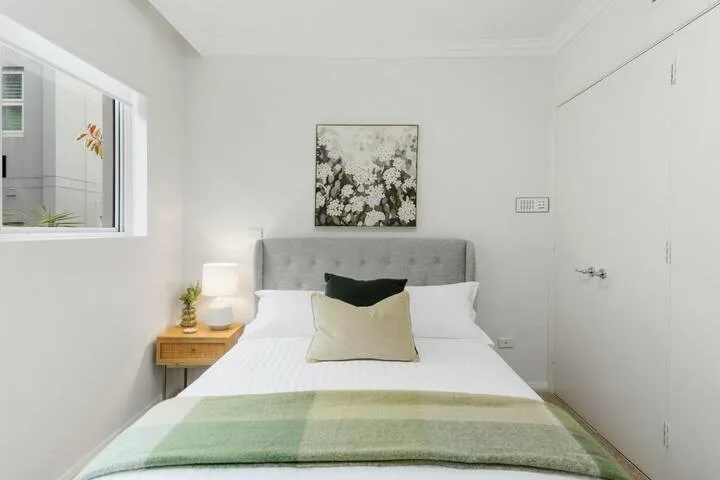 Dormitorio con una cama, un cabecero gris y un cuadro floral.